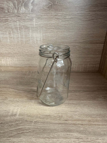 Etched hanging glass jar with floral design and metal handle on wooden background.