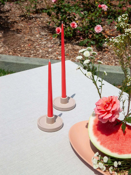 Moreton Taper Candle 25cm in Watermelon color on outdoor table with flowers and watermelon slice.